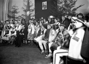 Kazimierz Przerwa-Tetmajer (siedzi w garniturze) w otoczeniu zespołu góralskiego na scenie, grudzień 1931 r., Kraków. Fot. Narodowe Archiwum Cyfrowe